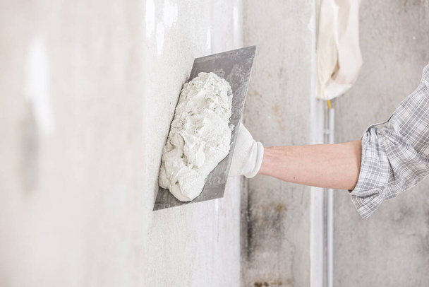 Bras d'un plâtrier tenant un nouveau plâtre pour un mur chargé sur une truelle de finition lors de travaux de rénovation ou de réparation de dégâts d'eau et de taches humides dans une maison
 - Photo, image