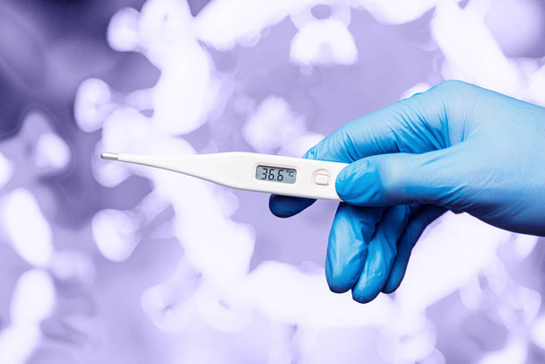 Медицинский работник в перчатках держит в руке электронный термометр на фоне изображения вируса
 - Фото, изображение