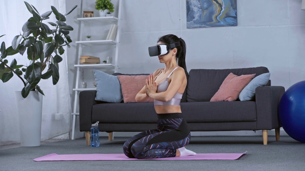 Seitenansicht des Sportlers im vr-Headset, der zu Hause auf der Fitnessmatte meditiert  - Filmmaterial, Video