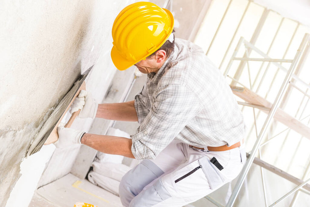 Construtor aplicando gesso novo em uma parede dentro de casa cobrindo uma mancha úmida durante renovações e reparos em uma imagem de close-up de chave alta
 - Foto, Imagem