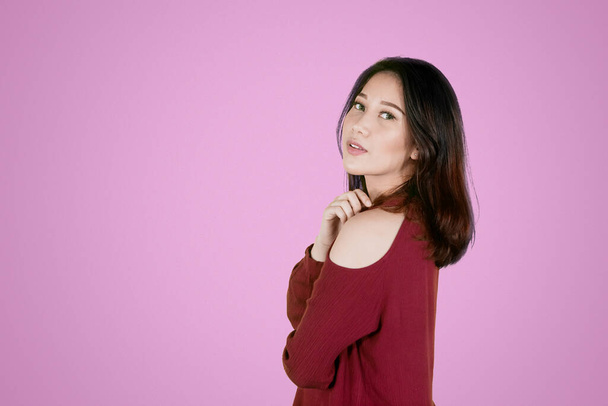 Portrait of beautiful young woman looking at the camera while standing and posing in the studio with pink background - Photo, image