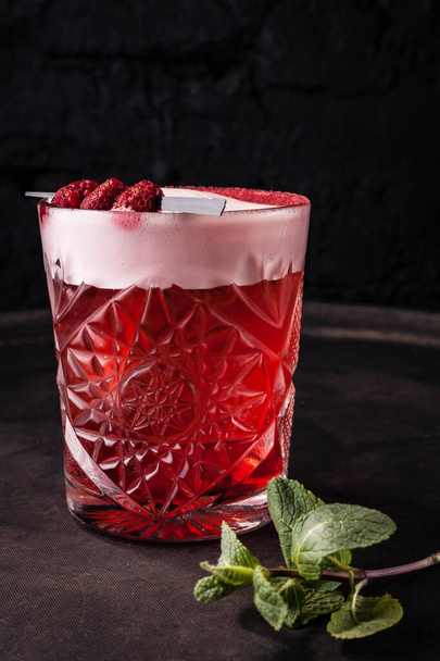 Cóctel de bayas rojas y dulces con espuma, decorado con frambuesas en un pincho en un vaso
. - Foto, Imagen