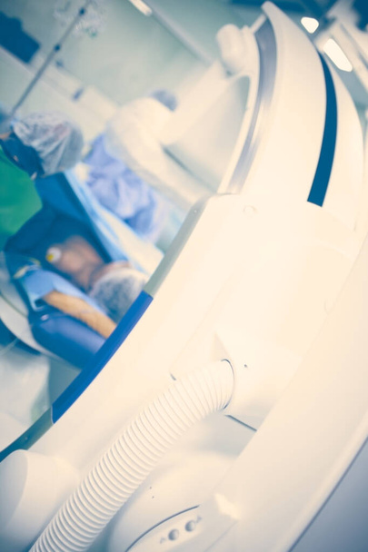 Patient in the x-ray room surrounded by health workers and modern equipment, blurred medical background. - Photo, image