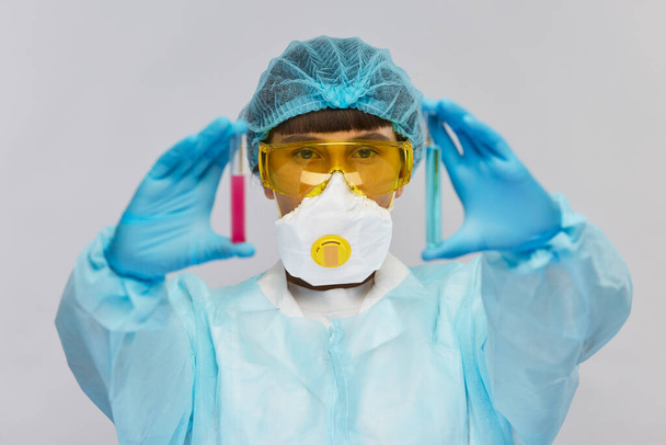 junge Wissenschaftlerin in medizinischer Einmalmütze und gelber Schutzbrille mit Reagenzgläsern mit blauen und rosa Flüssigkeiten - Foto, Bild