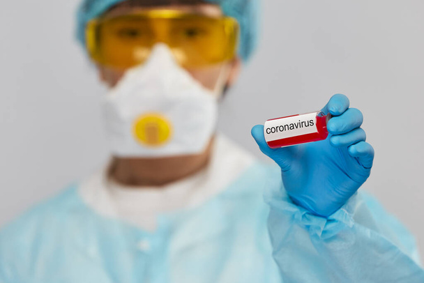 doctor in biohazard ptotective suit holding sample of coronavirus in test tube, young scientist with antivirus to COVID-19 - Foto, imagen