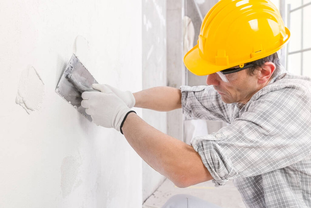 家の内装の白い壁の表面に新しい石膏を滑らかにするために仕上げのトロールを使用して左官やクローズアップビューで建設中 - 写真・画像