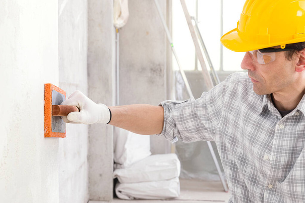 Construtor alisando novo gesso em uma parede interior usando uma ferramenta de esponja úmida em preparação para lixar e pintar durante reparos ou renovações
 - Foto, Imagem