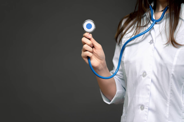 Ärztin mit Stethoskop in den Händen in Nahaufnahme auf dunklem Hintergrund. - Foto, Bild