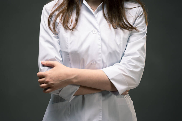 Doctor in medical gown is standing with crossed arms close up on dark background. - Фото, зображення