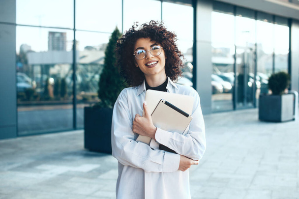 Lovely curly haired caucasian businesswoman is holding some gadgets and looking through eyeglasses - Foto, Bild