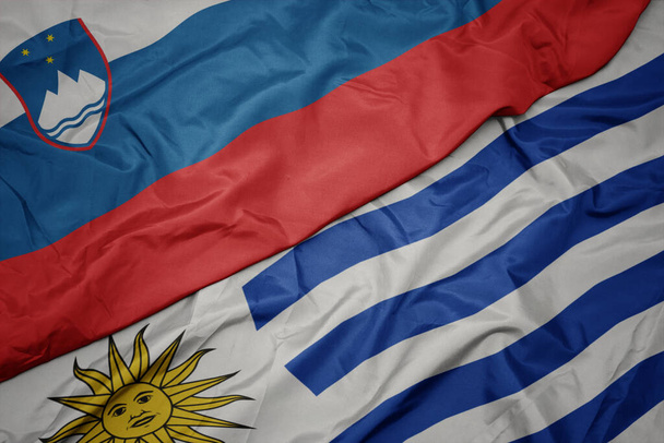acenando bandeira colorida de uruguai e bandeira nacional de slovenia. macro
 - Foto, Imagem