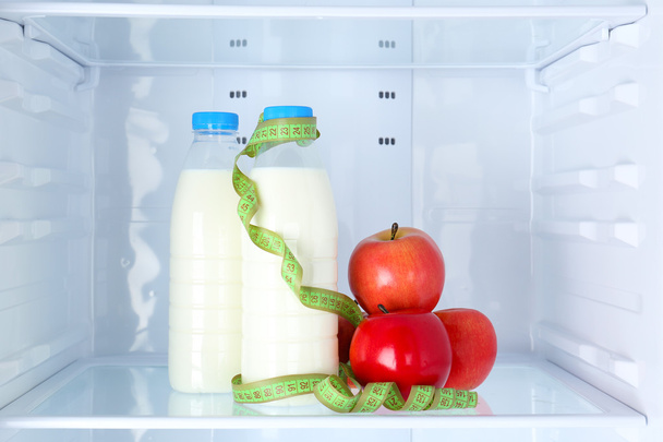 Conceptual photo of diet: apple and milk bottle with measuring type on shelf of refrigerator - Foto, Bild