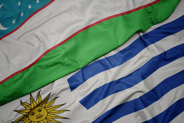 acenando bandeira colorida de uruguai e bandeira nacional do uzbequistão. macro
 - Foto, Imagem