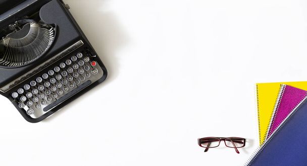 Ретро черная пишущая машинка, очки и ноутбуки разных цветов на белом фоне с копировальным пространством для текста
.  - Фото, изображение