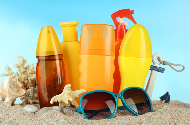 Bottles with suntan cream and sunglasses, on blue background - Photo, Image