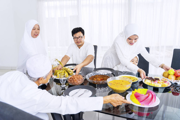 Portrait of cheerful muslim family eating together in dining room while celebrating eid mubarak  - Photo, Image