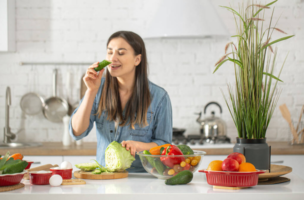 Μια νεαρή όμορφη γυναίκα ετοιμάζει σαλάτα με διάφορα λαχανικά στην κουζίνα. Η έννοια της υγιεινής διατροφής και του τρόπου ζωής. - Φωτογραφία, εικόνα