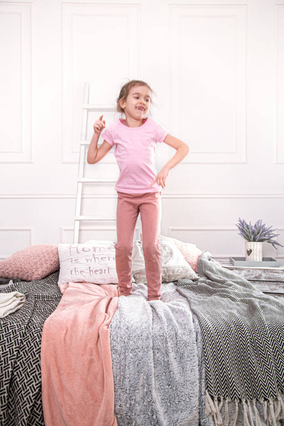 Roztomilá holčička si hraje na posteli. Skákání a baví. - Fotografie, Obrázek