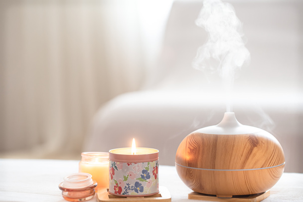 Moderne olie aroma diffuser in de woonkamer op de tafel met brandende kaarsen. Het concept van het verfrissen en zuiveren van de lucht in huis. - Foto, afbeelding