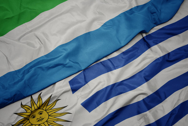 ondeando colorida bandera de uruguay y bandera nacional de sierra leona. macro
 - Foto, Imagen