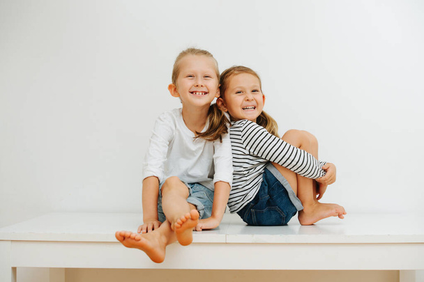 emotional portrait of 5 and 7 year old blond sibling sitting at home on a table  - Photo, Image