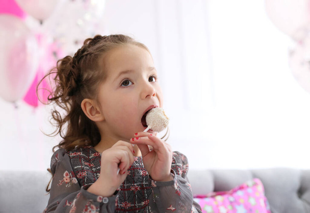 pretty curly girl in a gray flower dress eats candy on a stick with pleasure - Photo, Image