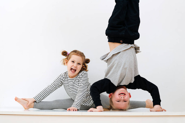 Portrait of children 5 and 7 years old, brother standing on his head and sister sitting on twine on a white background - Fotoğraf, Görsel