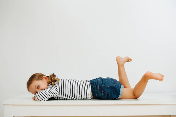 Girl in shorts and striped clothes lying on the table laughing and dangling legs - Foto, Bild