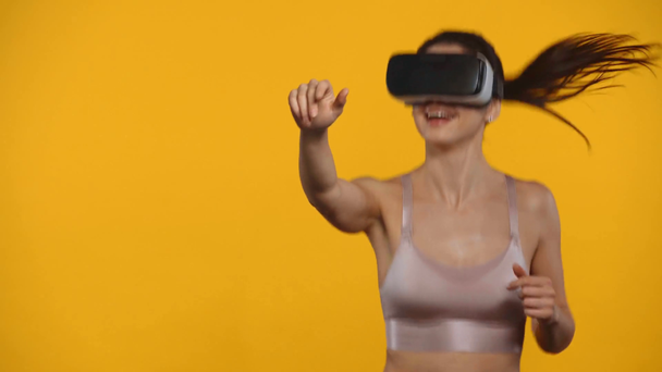 Lächelnde Sportlerin im vr-Headset joggt isoliert auf gelb - Filmmaterial, Video