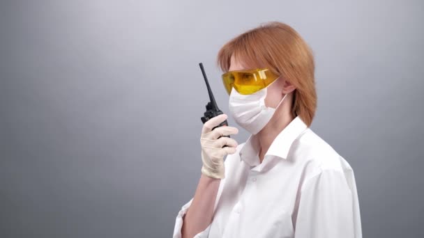biztonsági szemüveges nő, orvosi maszk és gumikesztyű beszél a rádión, vagy beszél egy hordozható rádión. 4k. Coronovírus és védelem. COVID-19 szám. - Felvétel, videó