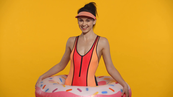 Mosolygós lány fürdőruhában úszógyűrűt tart elszigetelve a sárgán - Felvétel, videó