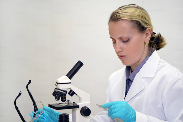 Scientist looks at a test sample. Side view of confident female scientist using microscope while sitting at her working place. Medical technology and pharmaceutical research and development concept. - Photo, Image
