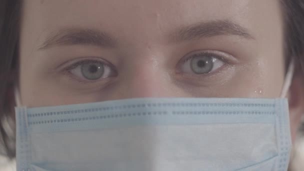 Extreme close-up of grey eyes of young woman in protective mask. Beautiful brunette Caucasian girl looking at camera. Quarantine measures, health care, isolation, safety. S-log 2. - Séquence, vidéo
