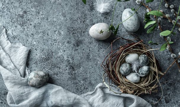 Marble Easter eggs in bird nest with feathers and spring flowers on blue background with napkin. Happy Easter holiday, top view, flat lay - Фото, изображение