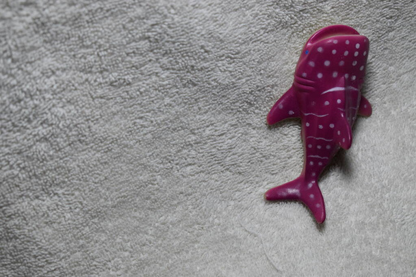 プラスチック製の子供のおもちゃのジンベエザメ紫色のピンクの肌、白い斑点、フィンと尾が白いテリークロスタオル素材に休んでいる. - 写真・画像