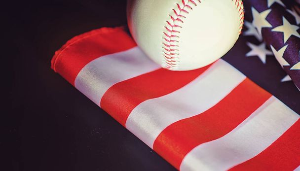Традиційна американська спортивна гра. Бейсбол. Концепція. Бейсбольний м'яч і кажани на столі з американським прапором.. - Фото, зображення