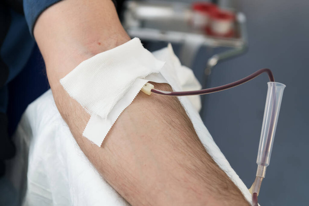 Sluit de arm van een man die bloed doneert. Een mannelijke donor geeft bloed in een mobiel bloeddonatiecentrum. Donatie om te ondersteunen tijdens een pandemie van coronavirus, selectieve focus. Wereldbloeddonordag - Foto, afbeelding