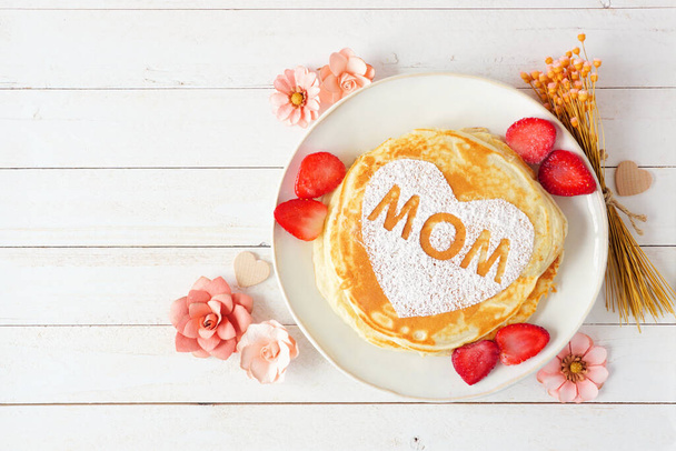 Pancakes with heart shape and MOM letters. Mothers Day breakfast concept. Overhead view against a white wood background. - Fotó, kép