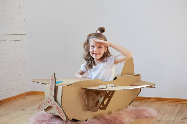 Little dreamer girl playing with a cardboard airplane. Childhood. Fantasy, imagination. - Foto, imagen