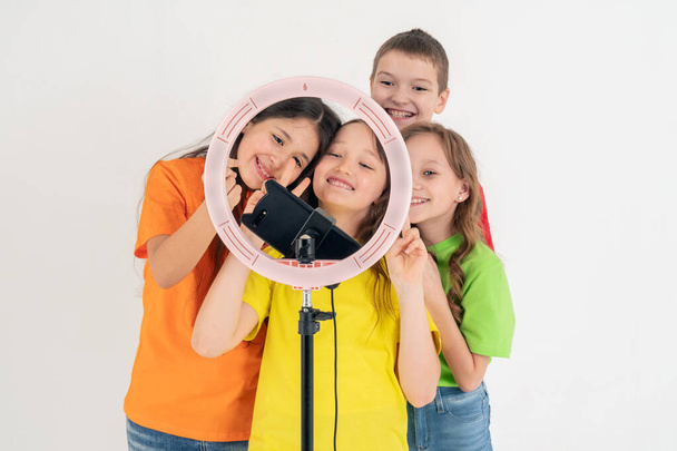Drie tienermeisjes en een jongen die glimlacht en een video maakt. Selfies. De telefoon is gemonteerd op een statief en de ringlamp schijnt. - Foto, afbeelding
