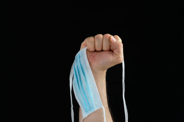 Pięść podnosząca maskę w symbolu walki z koronawirusem na czarnym tle - Zdjęcie, obraz