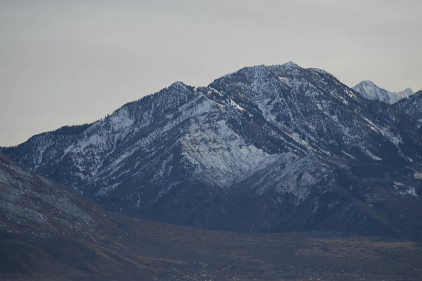 cime di montagna scure con neve, cielo nuvoloso nebbioso e colline pedemontane marroni
. - Foto, immagini