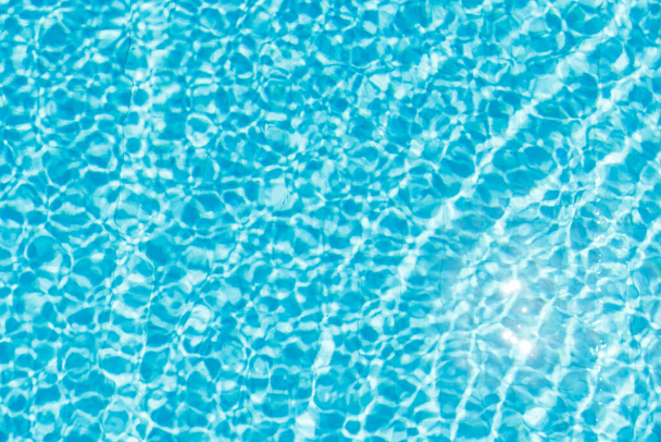 Oberfläche des blau leuchtenden Schwimmbadwassers plätschert und reflektiert die Sonne - Foto, Bild