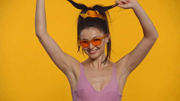 Cheerful girl in swimsuit showing thumbs up and heart signs isolated on yellow - Footage, Video
