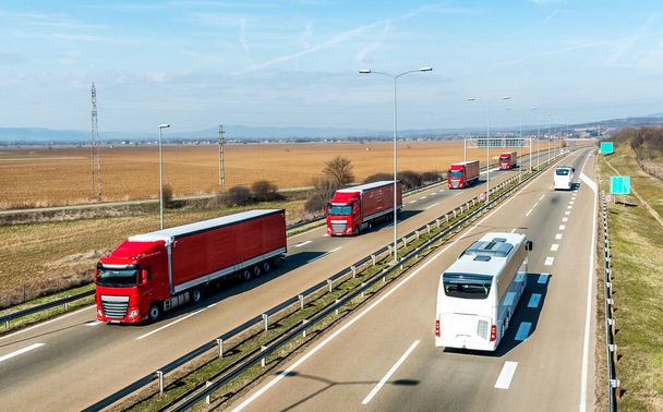 Convoy de transporte rojo Camiones en línea que pasan dos autobuses blancos en una carretera rural bajo un hermoso cielo azul
 - Foto, imagen
