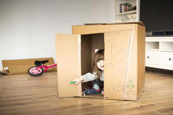Kleines Mädchen schaut beim Einzug in ein neues Haus aus einem Pappspielhaus. - Foto, Bild
