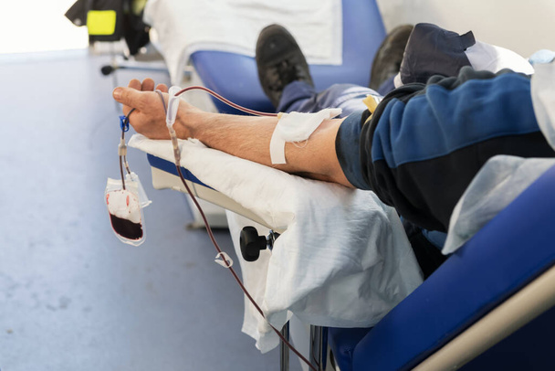 採血中に移動式の血液バンクのアームチェアに座っているドナーの手。コロナウイルス中の病院を支援するための寄付 - 写真・画像