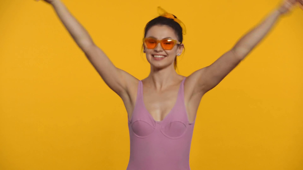Positive girl in swimsuit and sunglasses dancing isolated on yellow - Imágenes, Vídeo