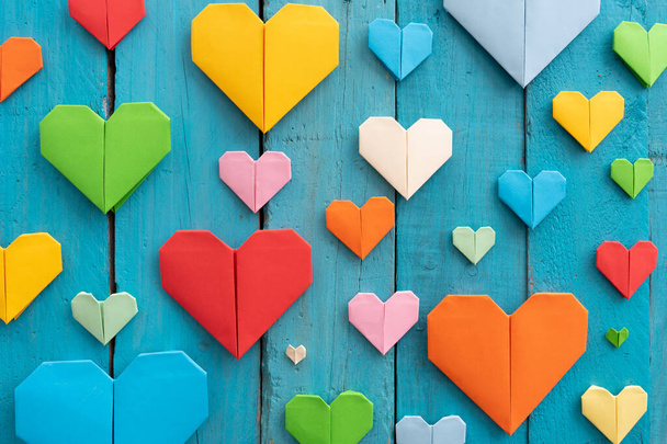 Origami hearts of different colors and sizes in composition on weathered blue wooden background - Фото, изображение