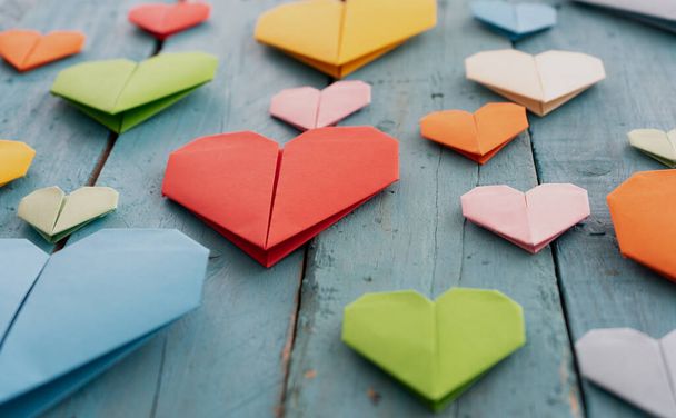 Origami hearts of different colors and sizes in composition on weathered blue wooden background - Fotó, kép